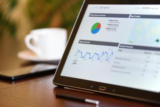 Tablet on a table with a coffee cup. On the tablet screen is several charts and graphs